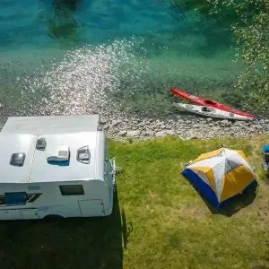 Aerial view of an RV, a tent and a kayak beside the water